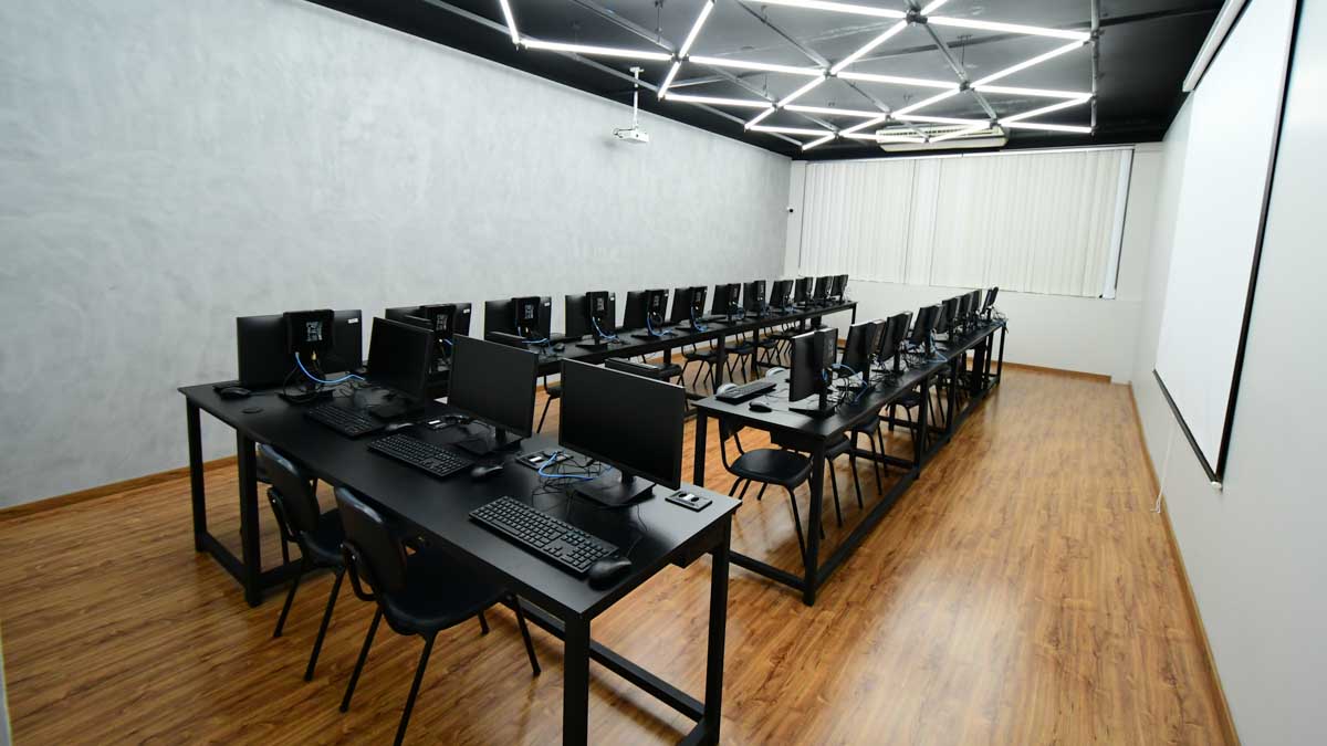 Laboratório de informática moderno e equipado para aulas do curso de Sistemas de Informação, com computadores e projetor, pronto para o ensino de tecnologia e programação.