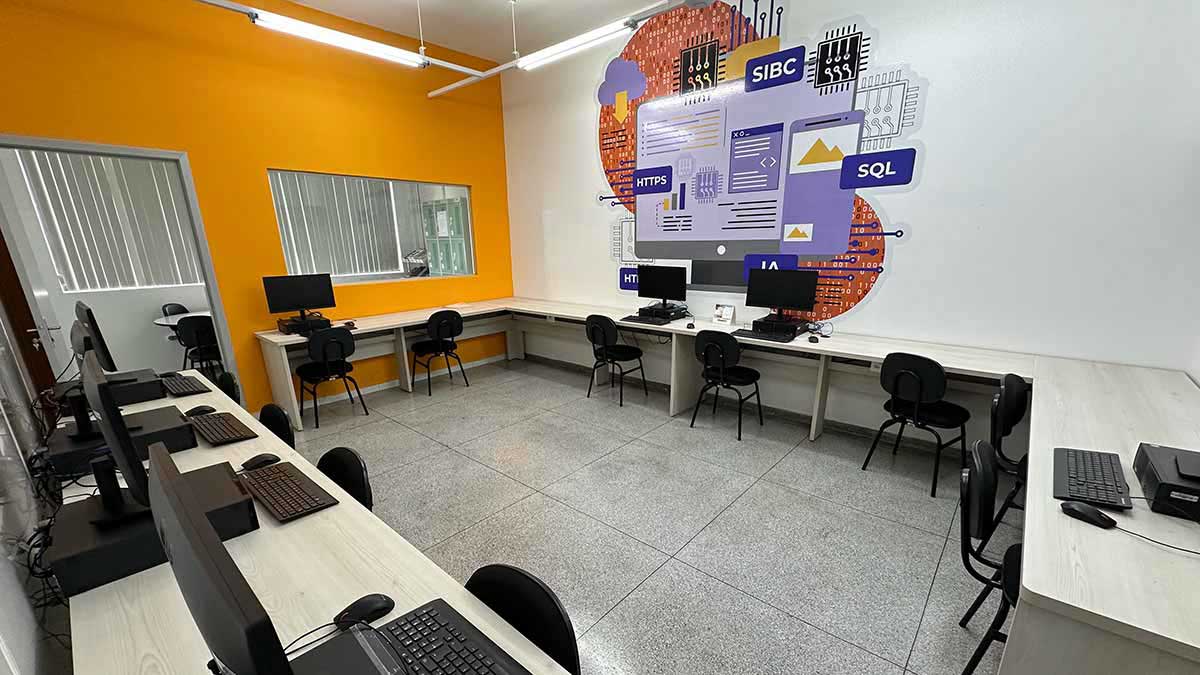Laboratório de informática equipado para o curso de Sistemas de Informação, com estações de trabalho e um mural ilustrando conceitos de programação e tecnologia, pronto para aulas práticas