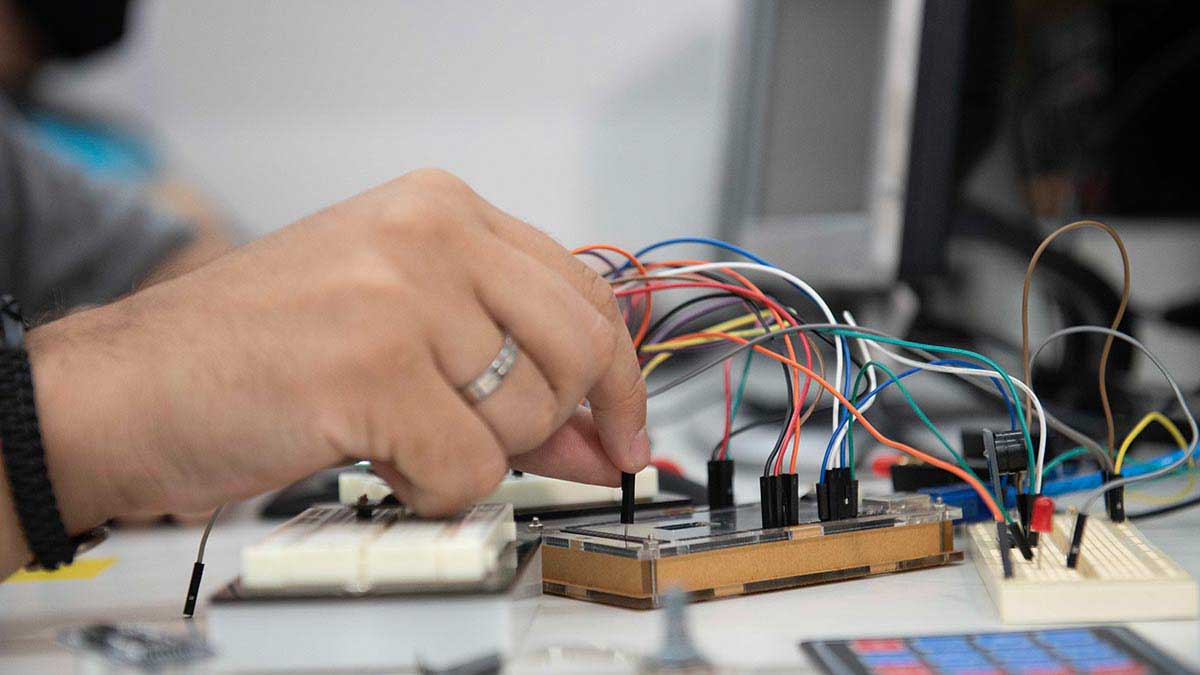 Aluno de Sistemas de Informação trabalhando com microcontroladores e eletrônica em laboratório, conectando componentes para prototipagem de sistemas embarcados e IoT