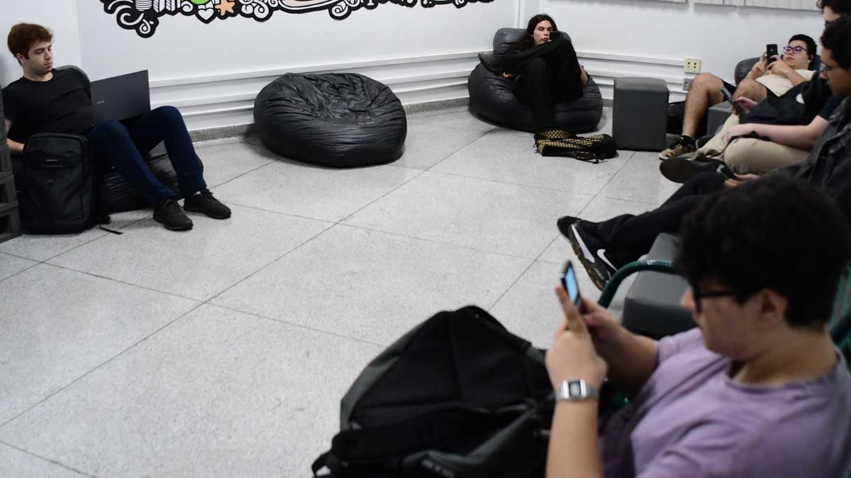 Alunos da faculdade de Sistemas de Informação relaxando e interagindo em uma sala de descanso aconchegante, equipada com pufes e espaço para estudo informal e networking.