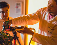 Alunos da Faculdade de Produção Sucroalcooleira em laboratório, analisando plantas com equipamentos de medição, focando em pesquisa e desenvolvimento.