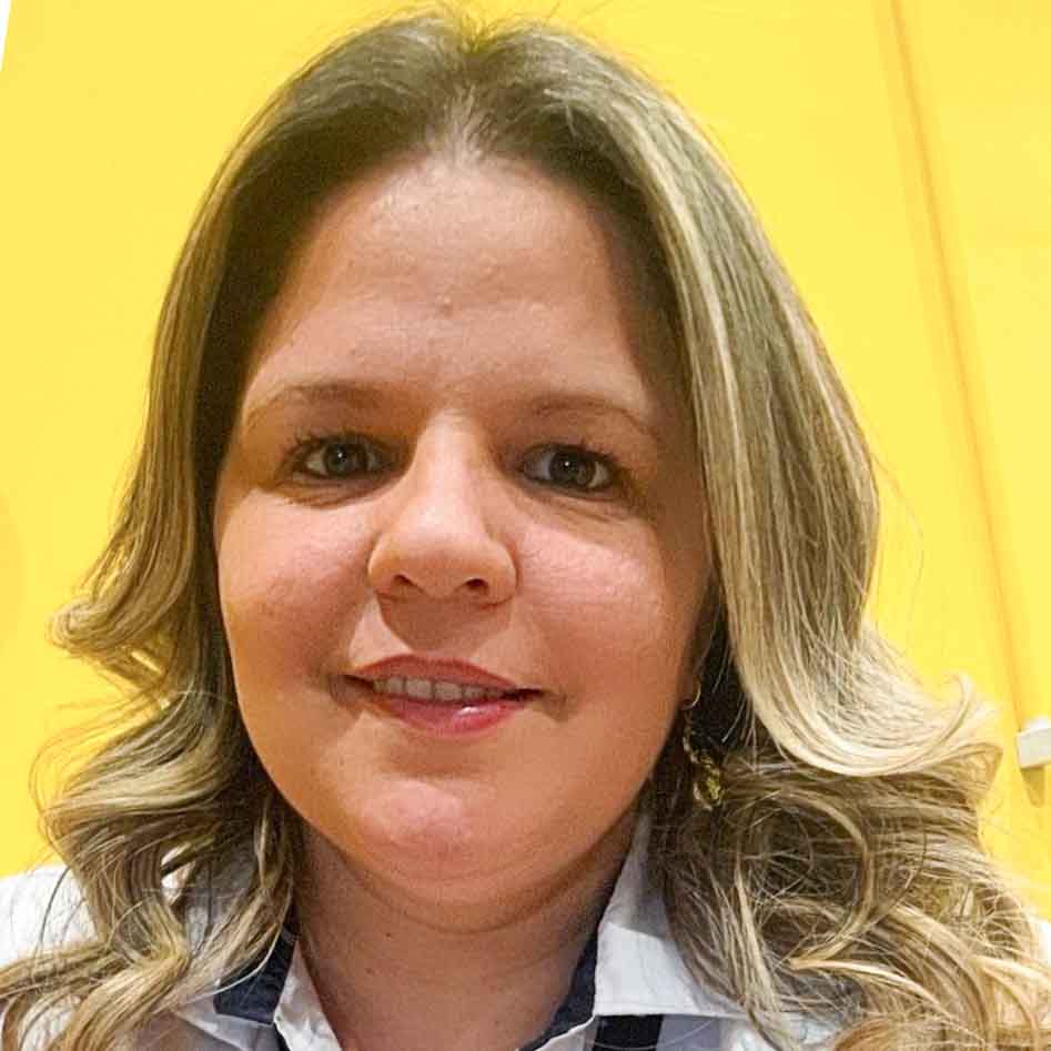 Tatiane, aluna do curso de gestão comercial, posando em um ambiente interno com uma parede amarela vibrante ao fundo. Seu cabelo ondulado com mechas claras adiciona destaque à composição.