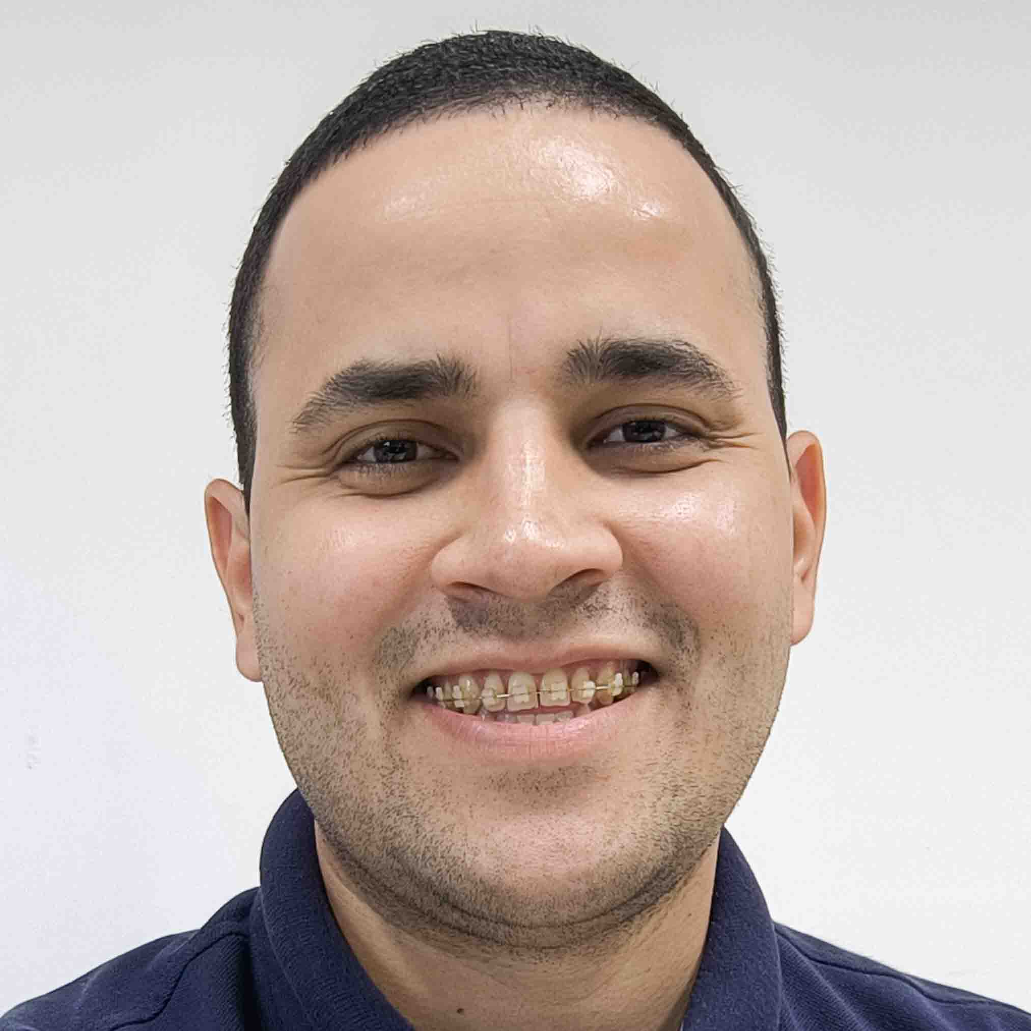 Vinícius, egresso do curso de gestão comercial, em um estúdio com fundo branco. Ele veste uma camisa azul escura, criando um contraste limpo e profissional.