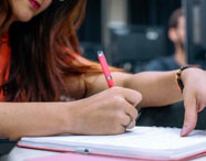 Aluna de Gestão Comercial concentrada em atividades de laboratório com caderno e caneta