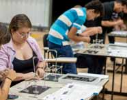Faculdade de Arquitetura em Presidente Prudente: aluna participa de aula prática em laboratório, montando estruturas arquitetônicas. O ambiente mostra mesas com materiais, outros alunos ao fundo e reforça a experiência prática do curso.
