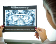 Aluna do curso de Odontologia segura com as duas mãos uma radiografia panorâmica de arcada dentária, próxima ao negatoscópio. A imagem mostra detalhes dos dentes e ossos maxilares. Ela usa touca, jaleco branco e esmalte vermelho nas unhas, demonstrando análise detalhada do exame.