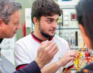 Grupo de alunos trabalha em conjunto no laboratório de instrumentação elétrica, manipulando fios e componentes em painéis didáticos. Os equipamentos apresentam mostradores, botões e conexões, fundamentais para o ensino prático no curso de Engenharia Elétrica.