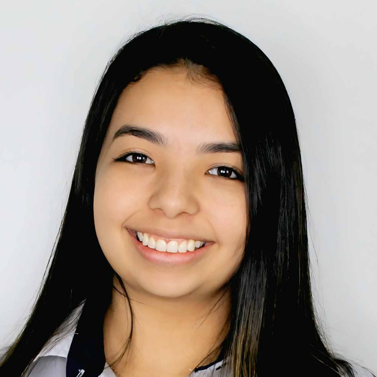 Thawane, egressa de Pedagogia, posando em um ambiente interno com um fundo claro. Ela tem cabelos longos e lisos, e usa uma camisa listrada, com um sorriso largo.