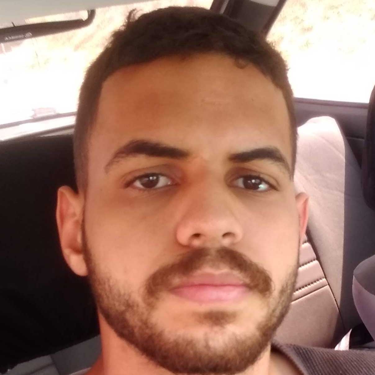 Claysson, egresso de Engenharia Mecânica, posando em um ambiente interno de carro. Ele tem barba e bigode, com uma expressão neutra.