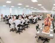 Amplo laboratório de anatomia repleto de alunos de Medicina em jalecos brancos, engajados em aulas práticas com diversos modelos anatômicos do corpo humano.