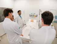 Professor de Medicina orientando três alunos em jalecos brancos em uma aula prática com um manequim de paciente em uma cama de hospital, discutindo um caso clínico.