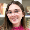 Imagem de Ana Paula, aluna do curso de medicina no campus Jaú, vestindo uma blusa rosa. O fundo apresenta prateleiras com modelos anatômicos e materiais de estudo, indicando um ambiente acadêmico técnico voltado para práticas médicas. A composição reflete organização e dedicação.