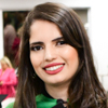 Imagem de Natália, egressa do curso de medicina no campus Jaú, vestindo beca preta de formatura com detalhes brancos e verdes. O fundo apresenta um ambiente interno iluminado, sugerindo um momento de celebração e reconhecimento pela conclusão de sua jornada acadêmica.