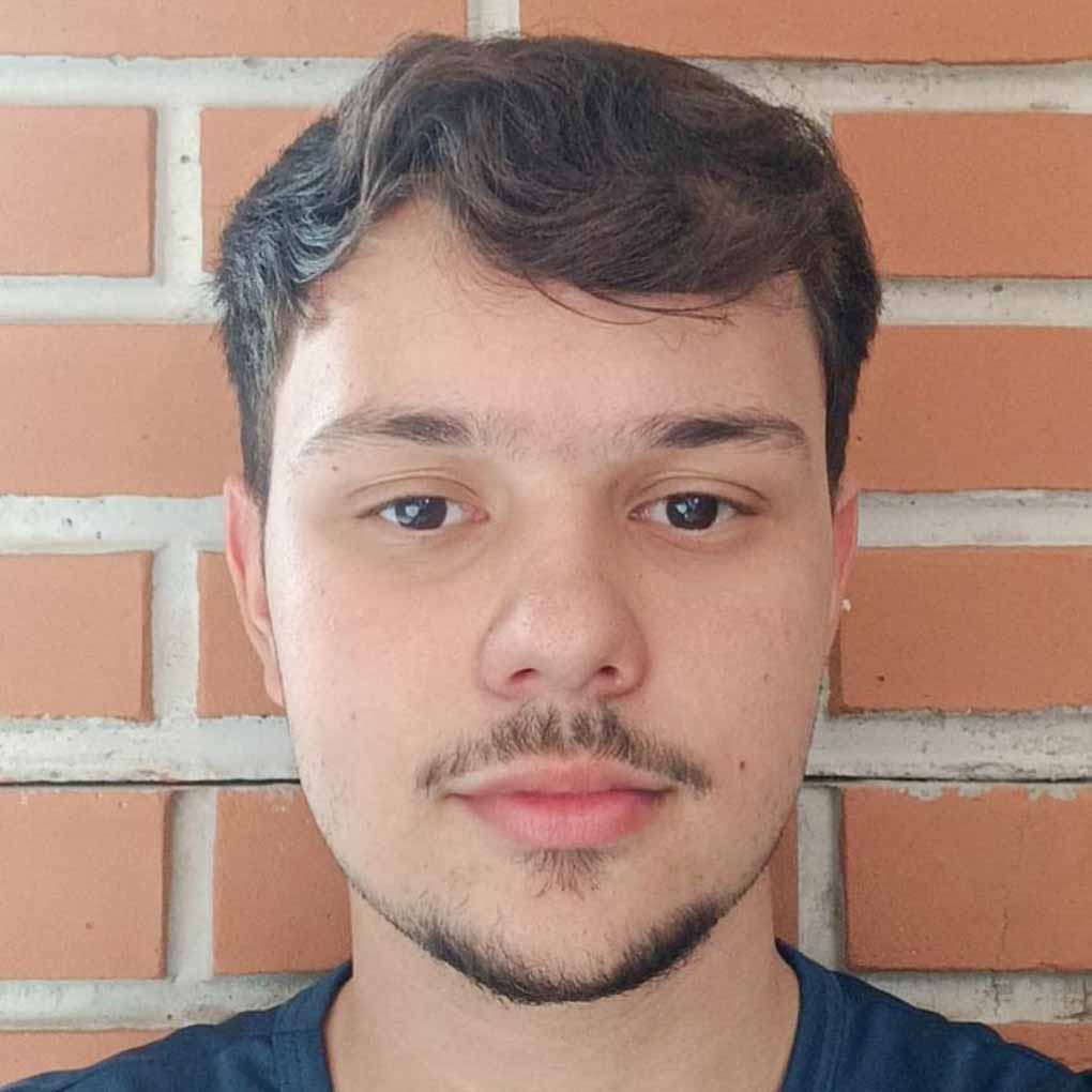 Davi, aluno de Engenharia Civil, posando em um ambiente interno com uma parede de tijolos ao fundo. Ele tem barba rala e uma expressão neutra.