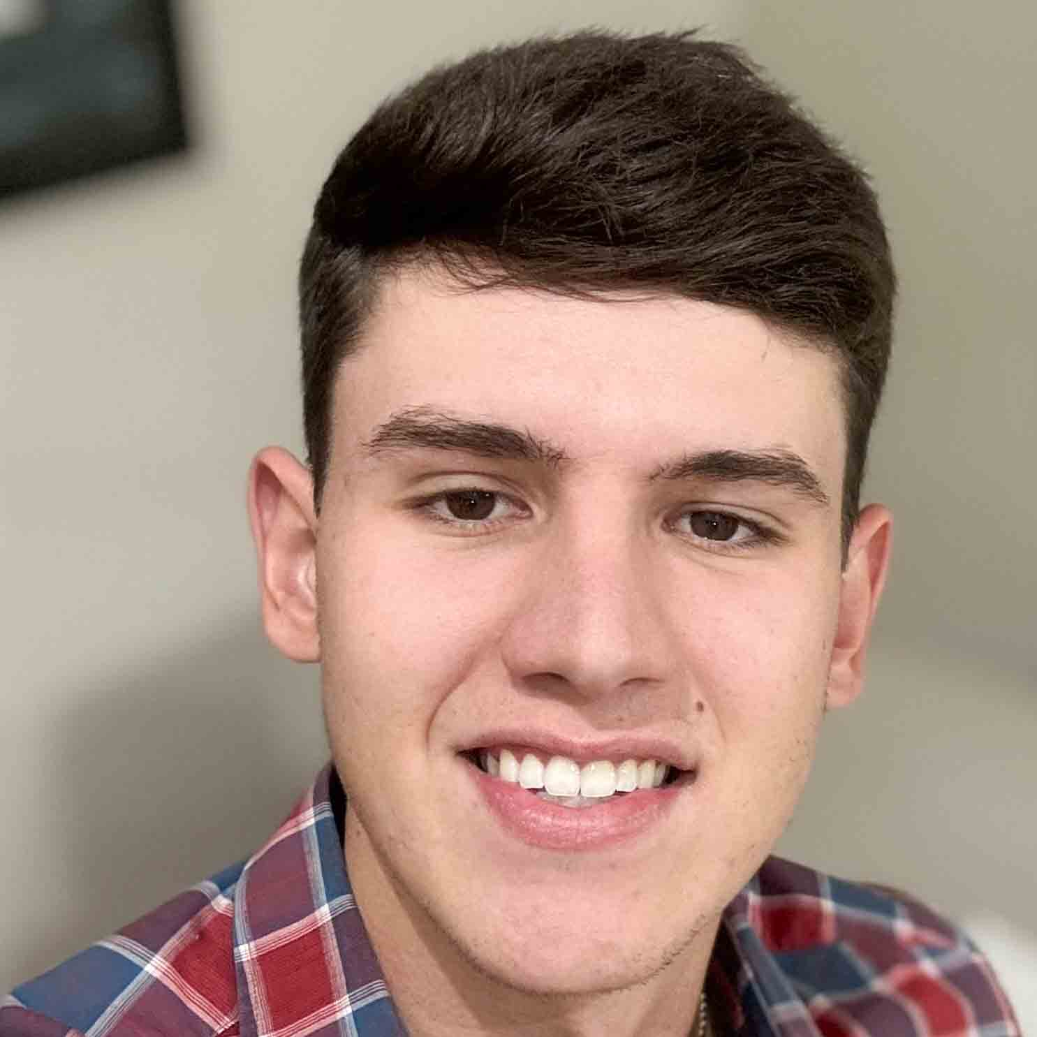 Guilherme, aluno de Engenharia Civil, posando em um ambiente interno com um fundo claro. Ele usa uma camisa xadrez e tem cabelos curtos, com um sorriso largo.