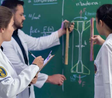 Estudantes do curso de Engenharia Civil, usando jalecos brancos com brasão do curso, analisam fórmulas e desenhos técnicos em um quadro verde. Um aluno segura régua de madeira junto ao desenho de uma viga, enquanto outro faz anotações em prancheta, ilustrando aula prática sobre estruturas.