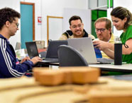Alunos da Faculdade de Gestão Ambiental recebendo orientação de professor, utilizando notebooks em ambiente de estudo colaborativo.