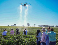 Grupo de alunos da Faculdade de Gestão Ambiental em Presidente Prudente observando drone agrícola em campo, demonstrando aplicação de tecnologia no meio ambiente.