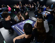 Alunos da Faculdade de Gestão Ambiental em aula na Sala Betha, utilizando mesas interativas para aprendizado tecnológico e colaborativo sobre temas ambientais.