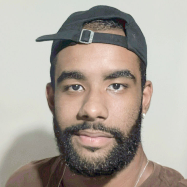 Daniel, aluno de Marketing, posando em um ambiente interno com um fundo claro. Ele usa um boné preto virado para trás e tem barba, com uma expressão neutra.