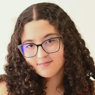 Izabela, aluna de Marketing, posando em um ambiente interno com um fundo claro. Ela usa óculos de armação preta e tem cabelos cacheados, com um sorriso suave.