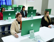 Laboratório de informática com fileiras de computadores iMac verdes, cada estação com teclado e mouse. Estudantes utilizam os equipamentos em ambiente claro, organizado e silencioso, reforçando o uso de tecnologia avançada na formação em Marketing da universidade.