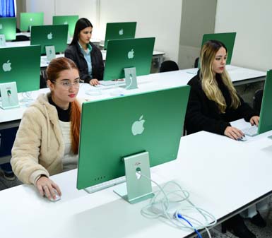 Sala de aula moderna com estudantes do curso de Marketing da instituição em Presidente Prudente, sentados em frente a computadores iMac verdes dispostos em fileiras. O ambiente é claro e organizado, com mesas brancas e cadeiras pretas, destacando o uso de tecnologia no ensino superior.