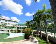 Pátio arborizado do campus 2 da Unoeste, com fonte vazia à esquerda, palmeiras alinhadas e edifícios acadêmicos ao fundo. Placa verde com o nome da instituição destaca a entrada principal, cenário típico das atividades de Engenharia Ambiental e Sanitária.