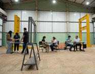 Aula prática acontecendo no laboratório de estruturas, com alunos reunidos ao redor do equipamento. 