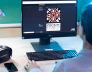 Pessoa trabalha em computador Dell em sala de Design Gráfico, visualizando mandala tipográfica e composição de texto na tela. Sobre a mesa, óculos de realidade virtual Warrior, luminária metálica e celular. Ambiente evidencia recursos tecnológicos aplicados ao ensino.