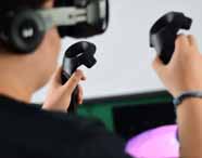 Aluno do curso de Design segura dois controles de realidade virtual enquanto utiliza óculos VR. A imagem destaca as mãos e os equipamentos tecnológicos, representando a integração de novas tecnologias digitais no ensino prático da Unoeste.