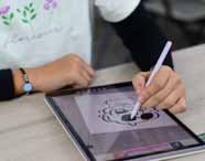 Estudante do curso de Design desenha em tablet com caneta digital, criando ilustração preta sobre fundo branco. Veste camiseta clara com flores e pulseira preta, praticando habilidades de ilustração digital em ambiente moderno e criativo.