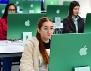 Estudante utiliza computador Apple em laboratório moderno no curso de Design. 