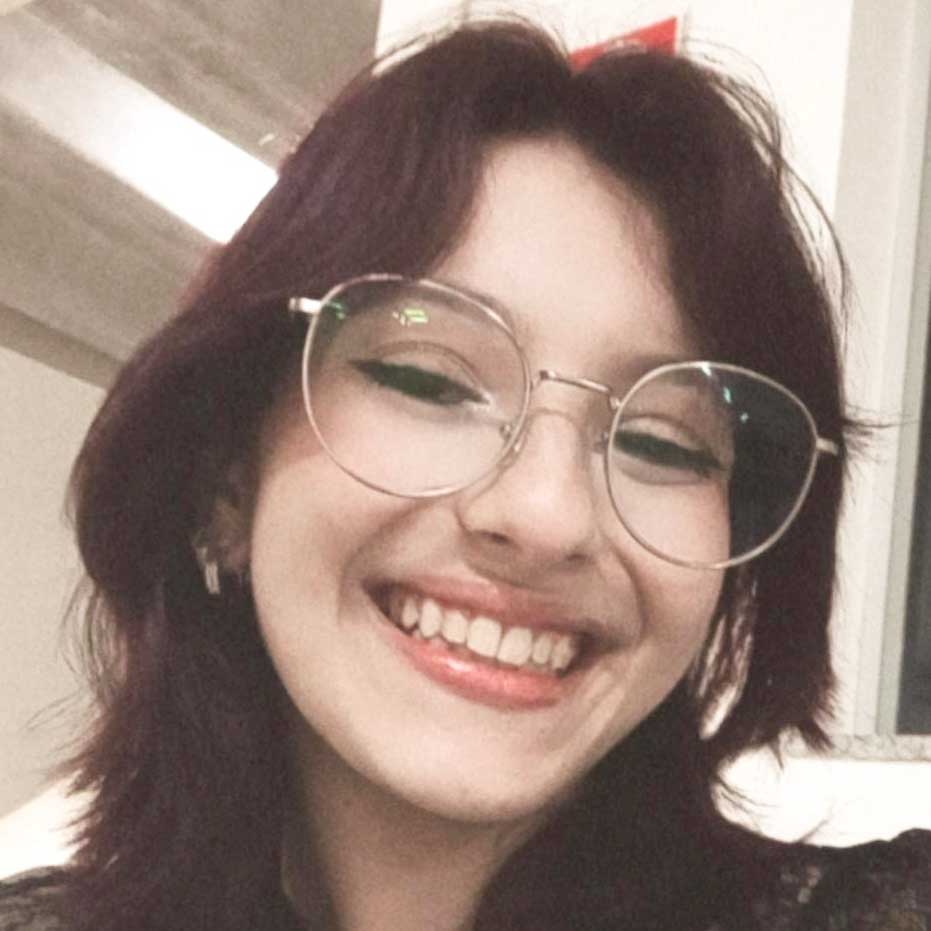 Ana Clara, aluna do curso de engenharia química, em um ambiente interno com iluminação suave e detalhes arquitetônicos modernos ao fundo. Ela usa óculos escuros que complementam seu estilo.