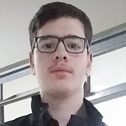 Heitor, aluno do curso de engenharia química, em um ambiente interno com janelas amplas ao fundo. Ele veste uma jaqueta preta, compondo um visual casual.