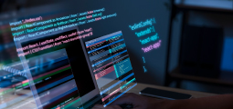 Visão aproximada em um ambiente escuro de uma tela de notebook exibindo blocos de código de programação. Sobreposta à tela e flutuando no espaço, há uma interface holográfica translúcida e brilhante com códigos de desenvolvimento web em texto colorido (azul, rosa e branco), exibindo comandos em React e blocos de configuração como "eslintConfig" e "react-app". No canto inferior direito, a mão de um desenvolvedor digita no teclado.