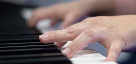 Close em duas mãos tocando simultaneamente as teclas brancas e pretas de um piano ou teclado. A imagem em profundidade de campo rasa destaca os dedos em contato com as teclas pretas ao fundo, transmitindo movimento e musicalidade.